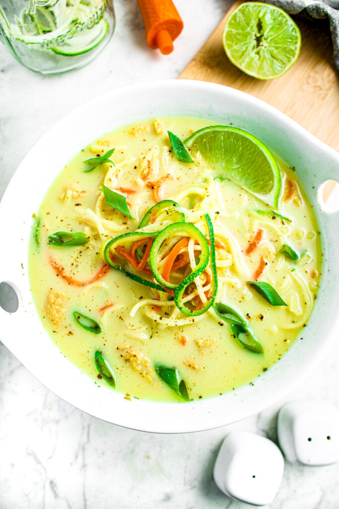 Overhead photo of a bowl of creamy green curry ramen garnished with a lime and zoodles