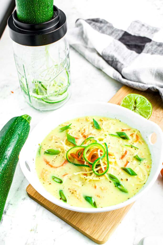 overhead photo of a bowl of zoodle ramen soup with a jar with Microplane spiralizer top on it in the background